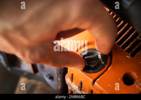 La mano svita il tappo del serbatoio dell'olio per la miscela lubrificante nella motosega arancione. Vista ravvicinata del serbatoio di lubrificazione della barra della catena della motosega Foto Stock
