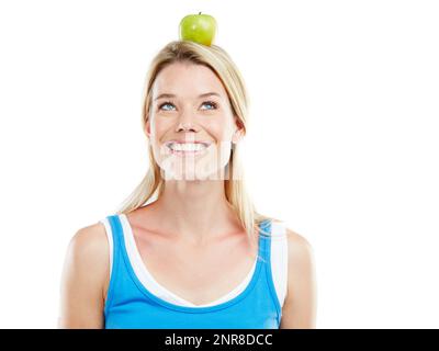 Mangiare bene è una forma di auto-rispetto. Studio shot di una giovane donna attraente con una mela sulla sua testa. Foto Stock