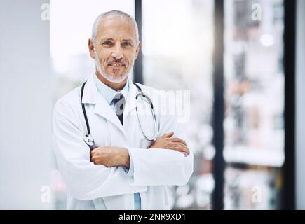 Im sicuro che posso curare che cosa li unga. Ritratto corto di un bel medico maturo in piedi con le braccia ripiegate in ospedale. Foto Stock