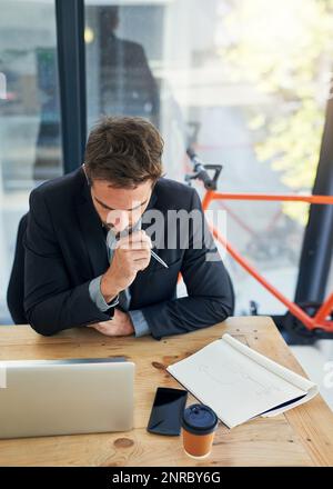 Ottenere le informazioni giuste per aiutarlo a riuscire. un bel giovane uomo d'affari seduto dietro il computer portatile nel suo ufficio. Foto Stock