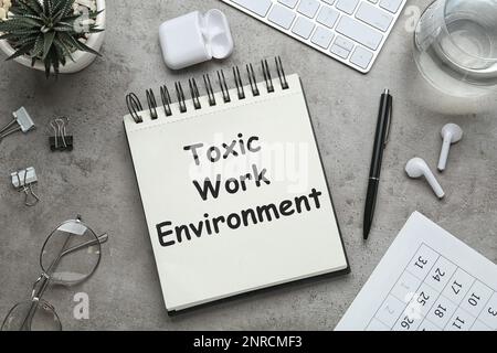 Notebook con testo Toxic Work ambiente su tavolo grigio, piano Foto Stock