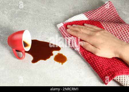 Donna che pulisce il caffè versato sul tavolo grigio, primo piano Foto Stock