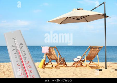 Termometro meteo e bella spiaggia di sabbia con lettini in legno sullo sfondo. Avviso corsa di riscaldamento Foto Stock