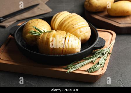 Patate Hasselback crude con rosmarino in teglia da forno su tavolo grigio scuro Foto Stock