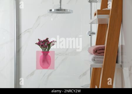 Vaso in silicone con fiori sul pannello in vetro della doccia in elegante bagno Foto Stock