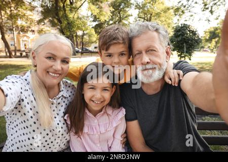 Nonni felici con bambini piccoli che prendono selfie nel parco Foto Stock