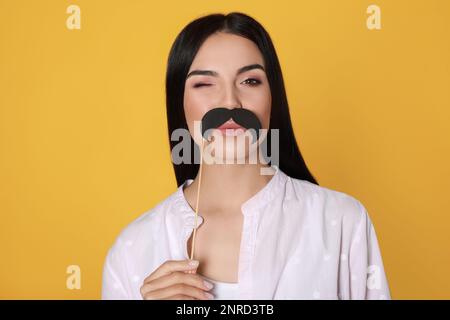 Donna divertente con baffi falsi su sfondo giallo Foto Stock