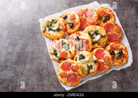 Mini pizza o pizzette assortite calde con vari condimenti primo piano su pergamena sul tavolo. vista orizzontale dall'alto Foto Stock