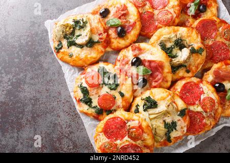 Pizza italiana Mini Pizza Bites con condimenti assortiti primo piano su pergamena sul tavolo. Vista orizzontale dall'alto Foto Stock