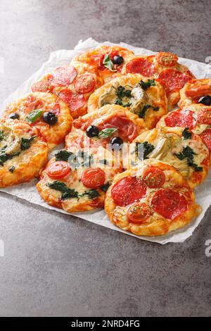 Mescolare la mini pizza o la pizzetta con vari condimenti primo piano sul pergamena sul tavolo. Verticale Foto Stock