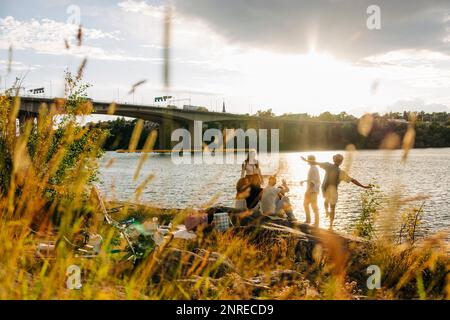 Amici di sesso maschile e femminile che trascorrono del tempo libero mentre si godono un picnic vicino al mare al tramonto Foto Stock