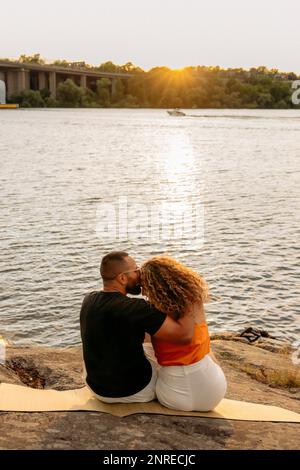 L'uomo bacia la ragazza mentre si siede sulla coperta da picnic vicino al mare Foto Stock