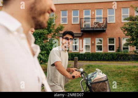 Giovane uomo che indossa occhiali da sole mentre si fa una passeggiata in bicicletta con un amico Foto Stock