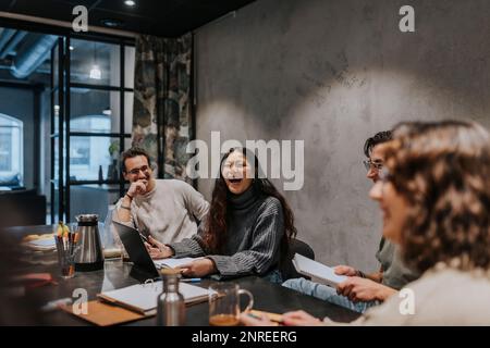 Allegri colleghi multirazziali che discutono al tavolo da conferenza nella sala riunioni Foto Stock