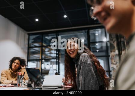 Giovane donna d'affari che ride mentre discute con i colleghi durante una riunione in sala riunioni Foto Stock