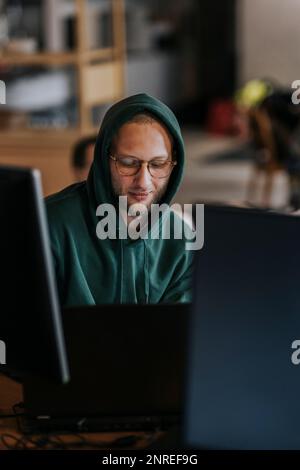 Giovane hacker maschio che lavora su un computer portatile in una società di startup Foto Stock