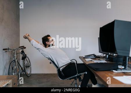 Un giovane hacker maschio che allunga le mani mentre lavora al computer in una società di startup Foto Stock