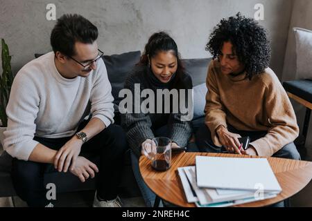 Giovane donna d'affari sorridente che discute su un tablet digitale con colleghi di sesso maschile e femminile in un ufficio creativo Foto Stock