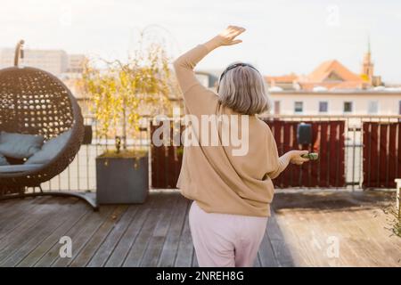 Vista posteriore della donna anziana che balla mentre ascolta la musica sulla terrazza Foto Stock