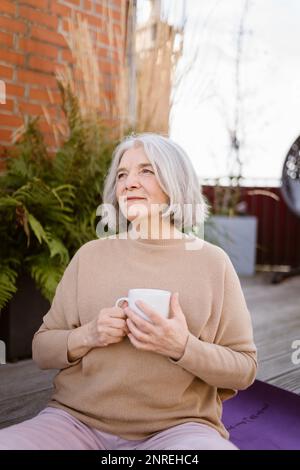 Donna anziana premurosa con tazza mentre si siede in terrazza Foto Stock