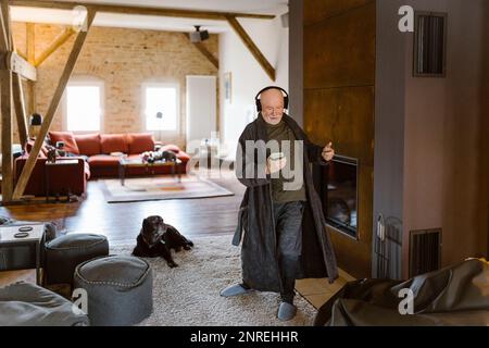 Un uomo anziano spensierato che balla e ascolta la musica mentre sta in piedi sul tappeto a casa Foto Stock