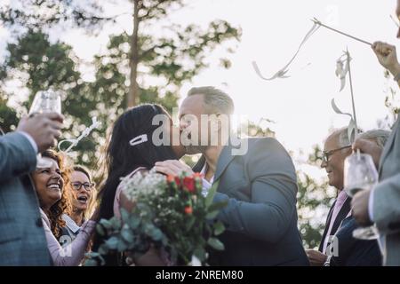 Coppia appena sposata che bacia in bocca da ospiti che li incoraggiano alla cerimonia di nozze Foto Stock