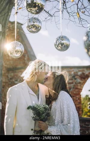 Coppia appena sposata che bacia in bocca sotto le palle da discoteca al matrimonio Foto Stock