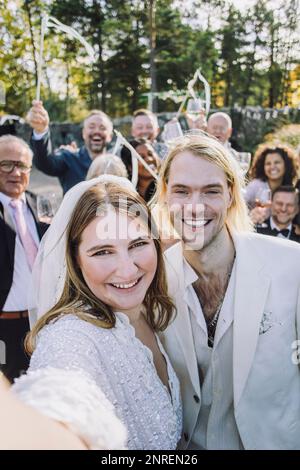 Ritratto di sposa felice prendendo selfie con sposo e famiglia il giorno di nozze Foto Stock