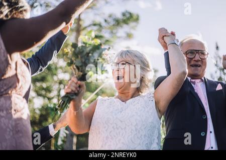 Coppia giovane giovane allegra che tiene le mani mentre balla con la famiglia il giorno del matrimonio Foto Stock