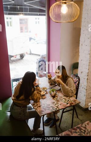 Vista ad alta angolazione delle amiche che comunicano mentre pranzano al ristorante Foto Stock