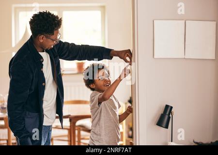 Buon padre e figlio che controllano l'altezza mentre si trovano vicino al muro a casa Foto Stock