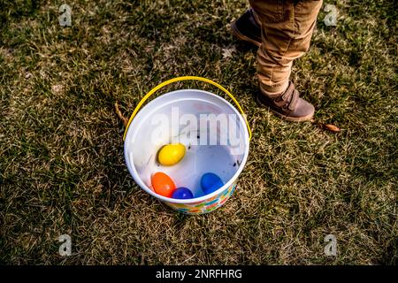 Ragazzo in piedi accanto al secchiello di plastica pieno di uova di pasqua colorate Foto Stock