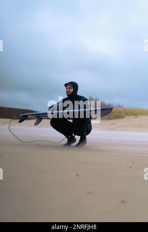 Surf a Kamchatka. Uomo in muta con tavola da surf sulla s Foto Stock