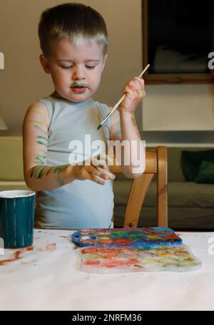 Il ragazzo è impegnato nella creatività: Dipinge le mani con la vernice Foto Stock