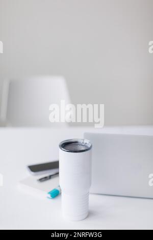 Spazio ufficio bianco con scrivania, computer e bottiglia bianca alta tazza Foto Stock