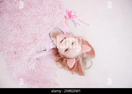 ragazza bionda con orecchie rosa giace sul pavimento rosa Foto Stock