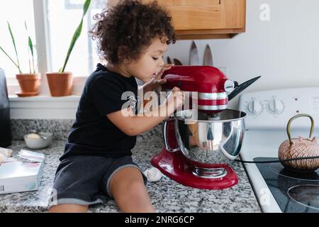 Bambino biraciale che sbircia nel recipiente di miscelazione dal bancone Foto Stock