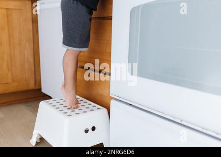 I toppy dei toddler's piedi sopra lo sgabello bianco per raggiungere il contatore Foto Stock