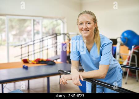 Giovane donna sorridente come fisioterapista in piedi in palestra di casa di cura Foto Stock