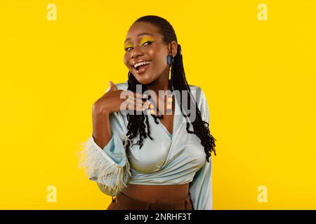 Splendida donna nera con trucco luminoso che posa su sfondo giallo Foto Stock