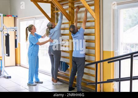 Fisioterapista femminile che assiste l'uomo anziano e la donna nell'esercizio presso il centro di riabilitazione Foto Stock