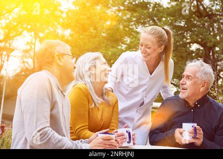 Felice gruppo di persone anziane ridere con l'infermiera all'aperto nel giardino di casa di cura Foto Stock