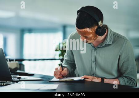 Ho bisogno di musica per farmi andare. un giovane uomo d'affari che fa la documentazione mentre indossa le cuffie in un ufficio al lavoro. Foto Stock