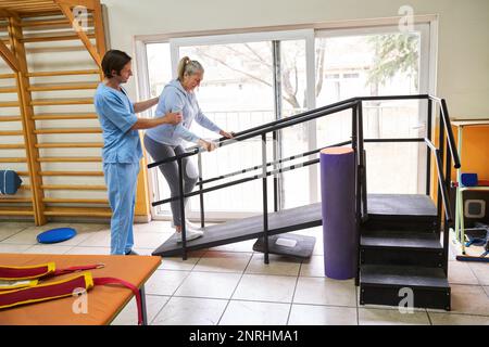 Fisioterapista maschile che assiste una donna anziana sulla rampa durante la terapia del movimento presso il centro di riabilitazione Foto Stock