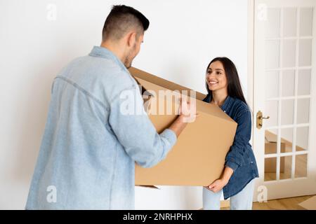 Felice giovane coppia che trasporta insieme la scatola di cartone, aiutandosi l'un l'altro nella giornata commovente Foto Stock