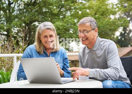 Coppia anziana felice che discute sopra il laptop al tavolo nel giardino della casa di cura Foto Stock