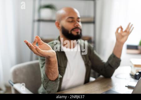 Rilassato uomo latino meditando di fronte al notebook e rilassandosi, rilassandosi con gli occhi chiusi sul posto di lavoro in ufficio a casa Foto Stock