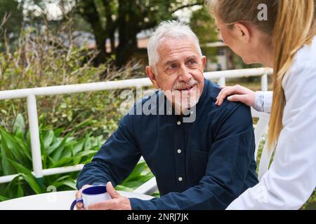 Donna medico consolante uomo anziano sorridente seduto in giardino di casa di cura Foto Stock
