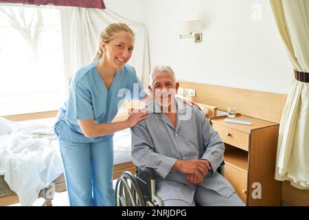 Ritratto di un caregiver sorridente con un anziano seduto in sedia a rotelle al centro di riabilitazione Foto Stock