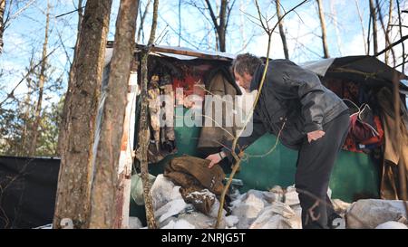 Un uomo senza casa passa attraverso le cose nella sua cabina nel bosco in inverno. Foto Stock